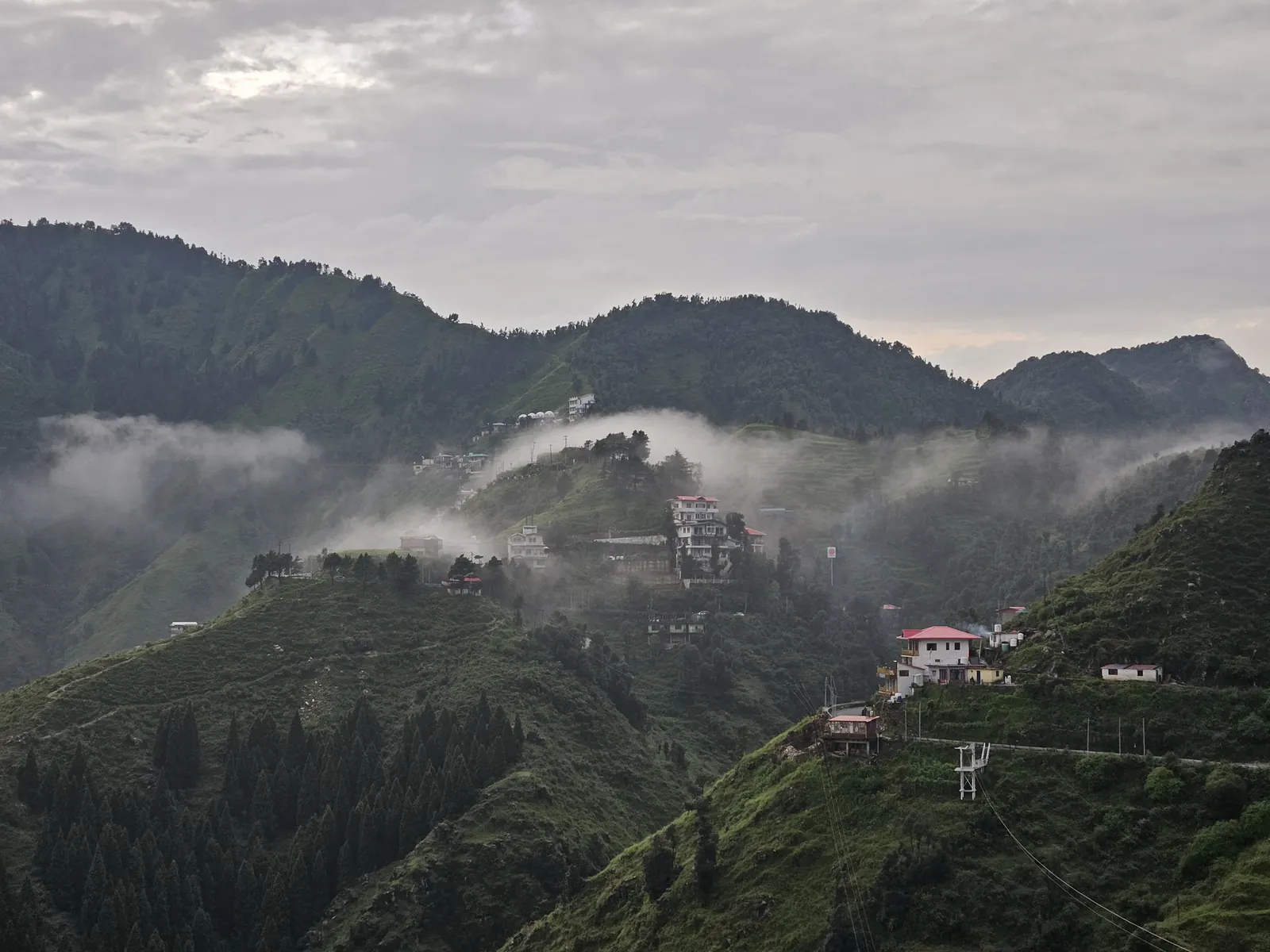 Mist and clouds rolling over green mountain slopes in Suwakholi, Uttarakhand, seen from Highlanders Café & Stay near Mussoorie
